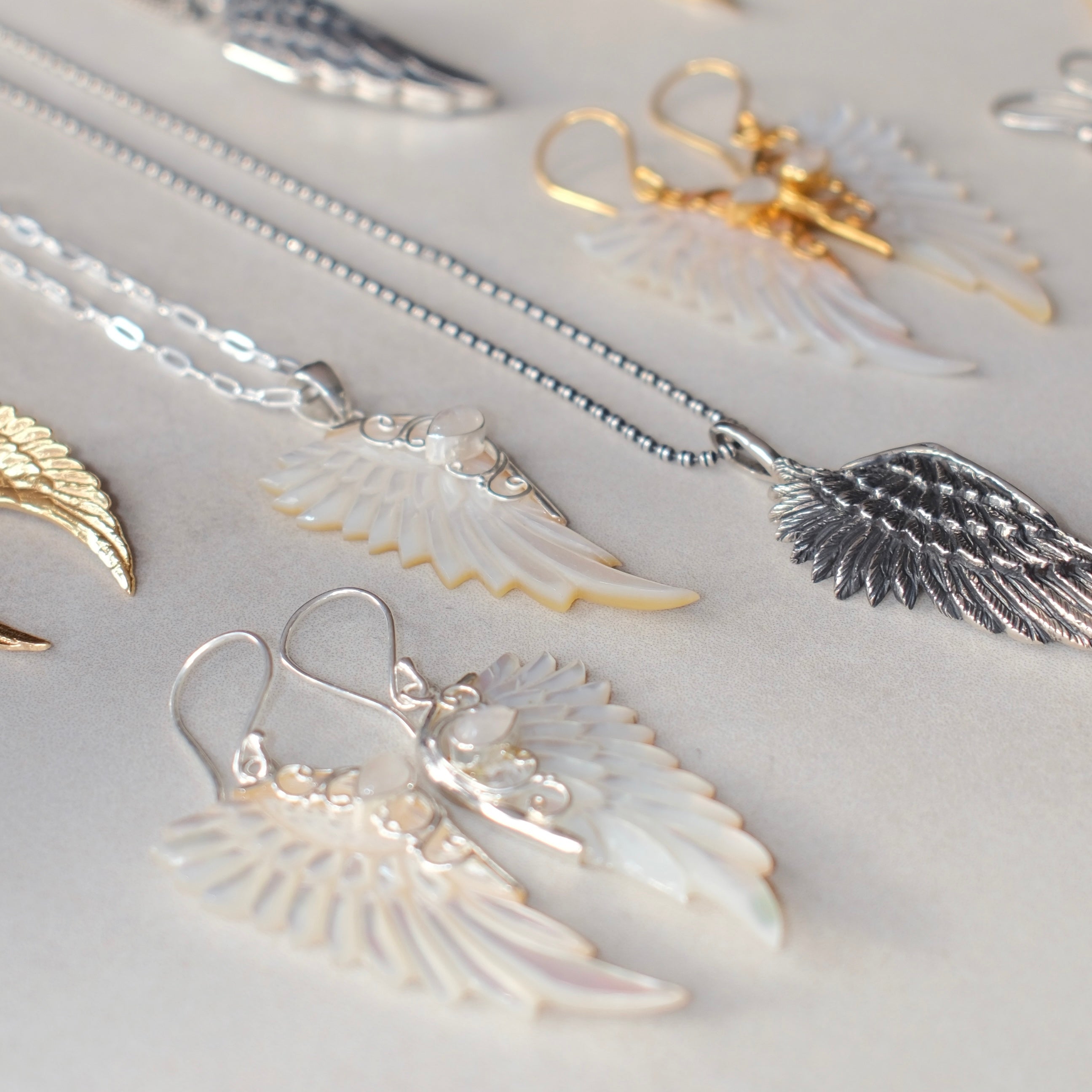 Sterling silver hand carved wing necklace with mother of pearl pendant and moonstone detail sterling silver chain, shown alongside other angel wing necklaces and earrings, statement jewellery by Angel Rocks