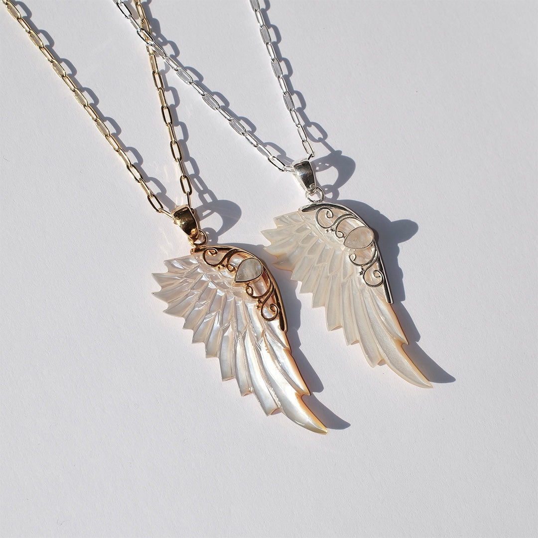 Gold and silver hand carved wing necklace with mother of pearl pendant and moonstone detail on 18kt gold plated sterling silver chain, shown alongside the silver hand carved wing necklace, statement jewellery by Angel Rocks