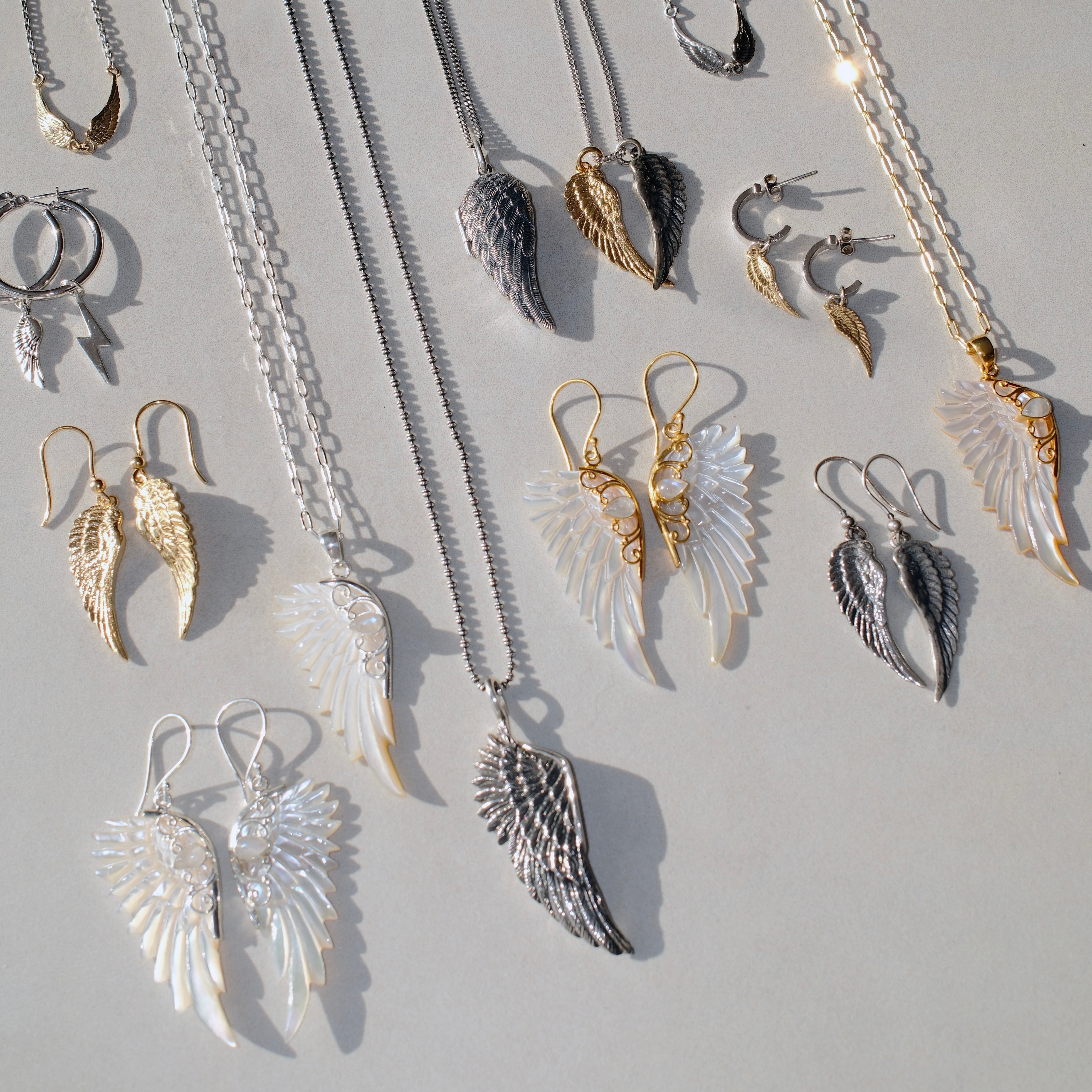 Gold hand carved wing necklace with mother of pearl pendant and moonstone detail on 18kt gold plated sterling silver chain, shown with other angel wing necklaces and earrings, statement jewellery by Angel Rocks
